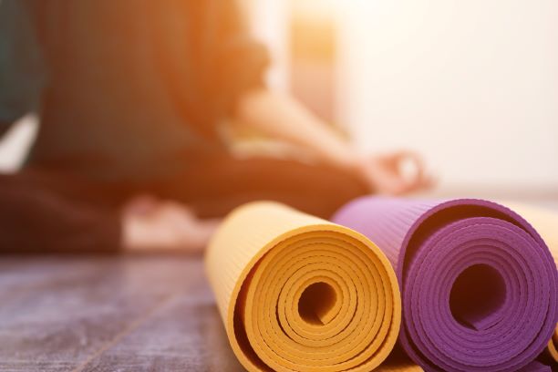 rolled yoga mats with female in backgroudn doing yoga pose