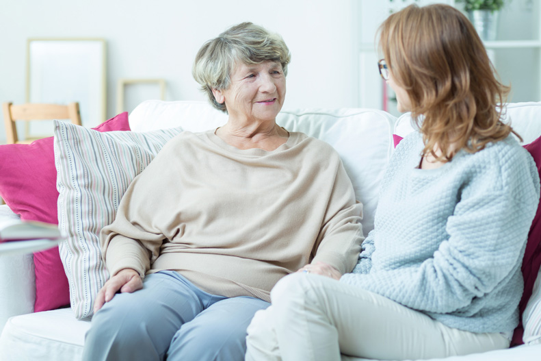 elderly woman and middle-aged woman sitting on couch talking