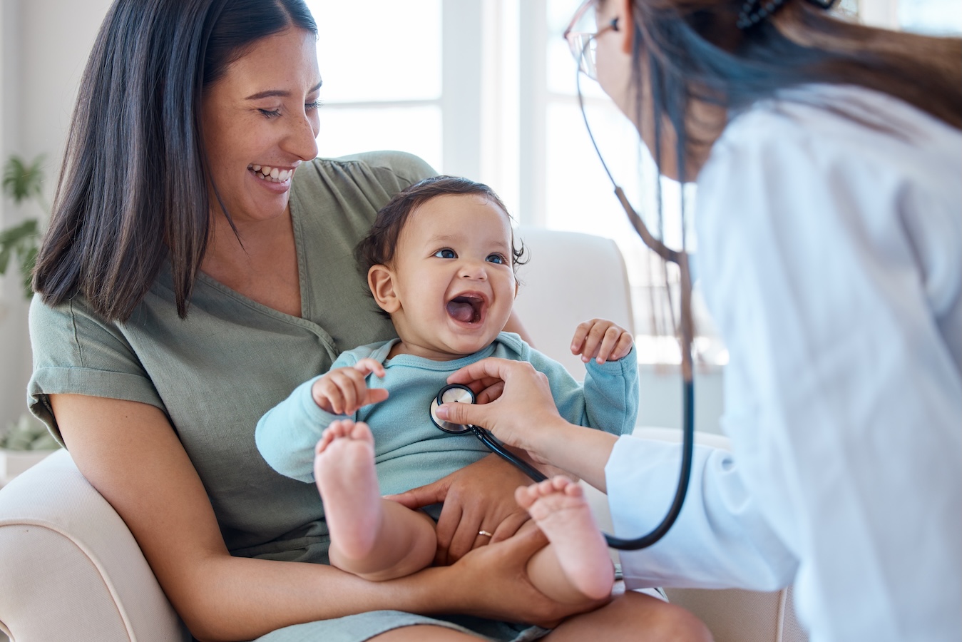 smiling mom and baby with doctor holding stethoscope to baby's chest